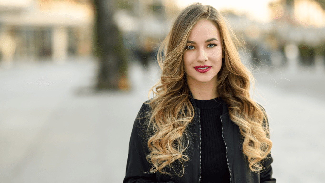 Young woman with long, curled blonde hair after a professional cut and blow-dry – representing longer hair styling at Cruz Hairworks in Whitley Bay.